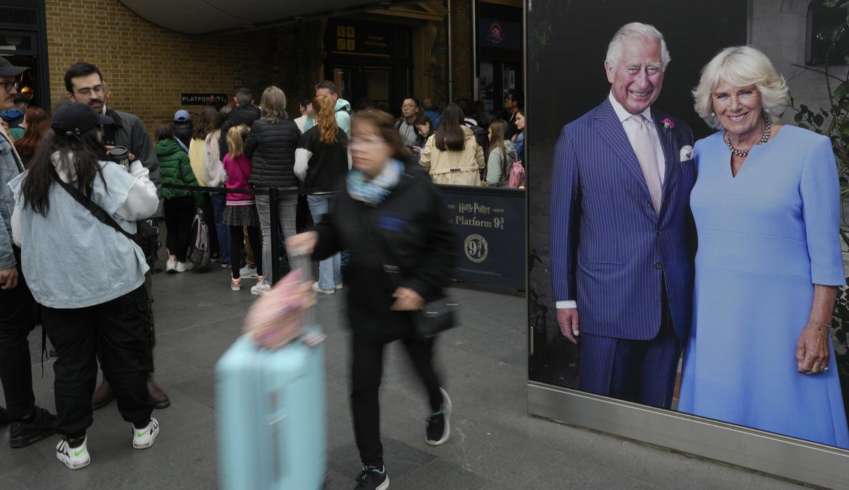 Wisatawan melewati potret besar Raja Charles III dan Ratu Camilla  yang dipajang di Stasiun Kings Cross di London, Senin, 1 Mei 2023. Penobatan Raja Charles III akan berlangsung di Westminster Abbey pada 6 Mei. (AP Photo/Kirsty Wigglesworth)