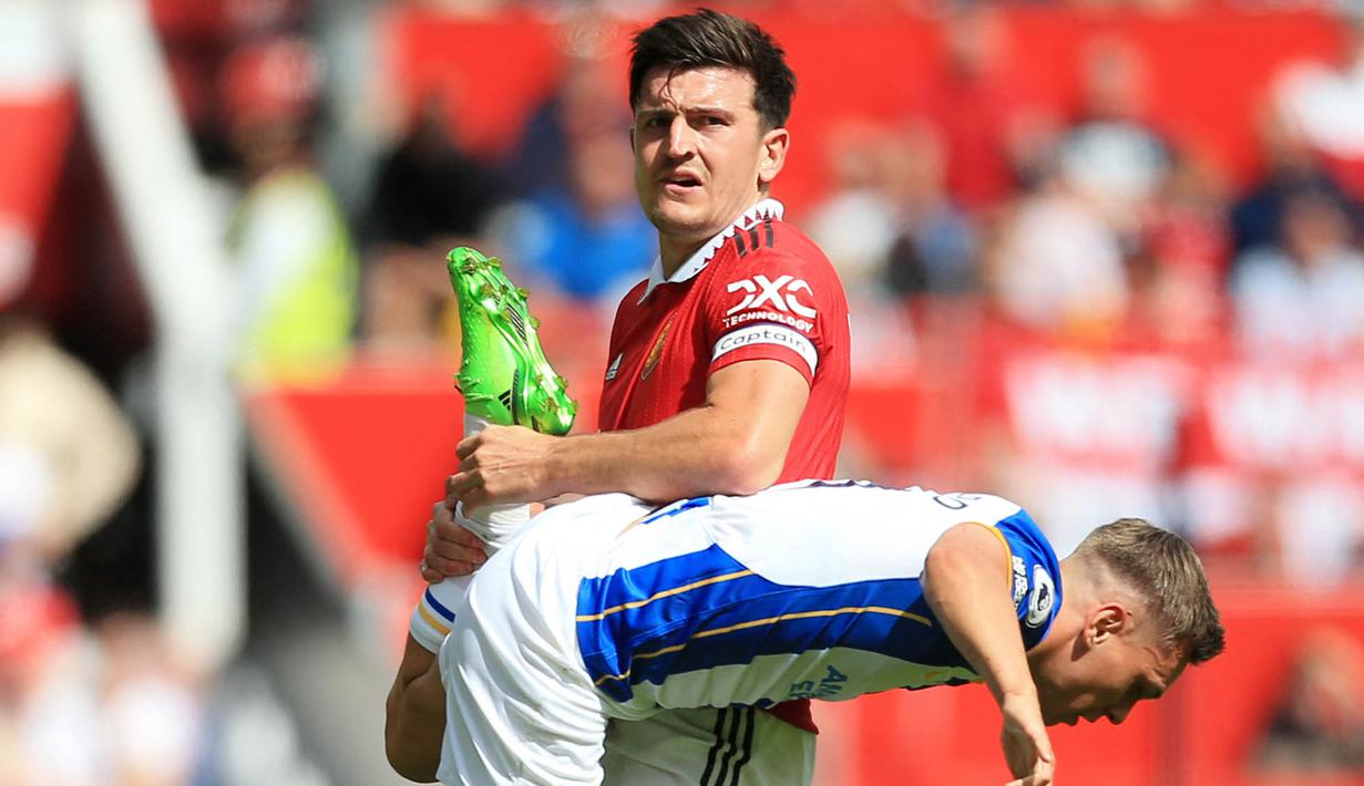 Bek Manchester United, Harry Maguire, mengangkat kaki pemain Brighton and Hove Albion, Leandro Trossard, pada laga Liga Inggris di Stadion Old Trafford, Minggu (07/08/2022). (AP/Lindsey Parnaby)