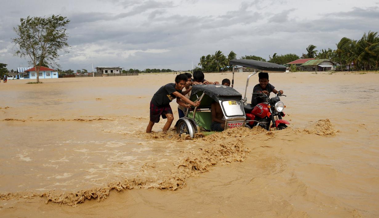 Sejumlah warga mendorong sebuah becak tradisional yang terjebak banjir di Nueva Ecija,  Filipina, Senin (19/10/2015). Badai terjadi pada Minggu pagi waktu setempat. (REUTERS/Erik De Castro)