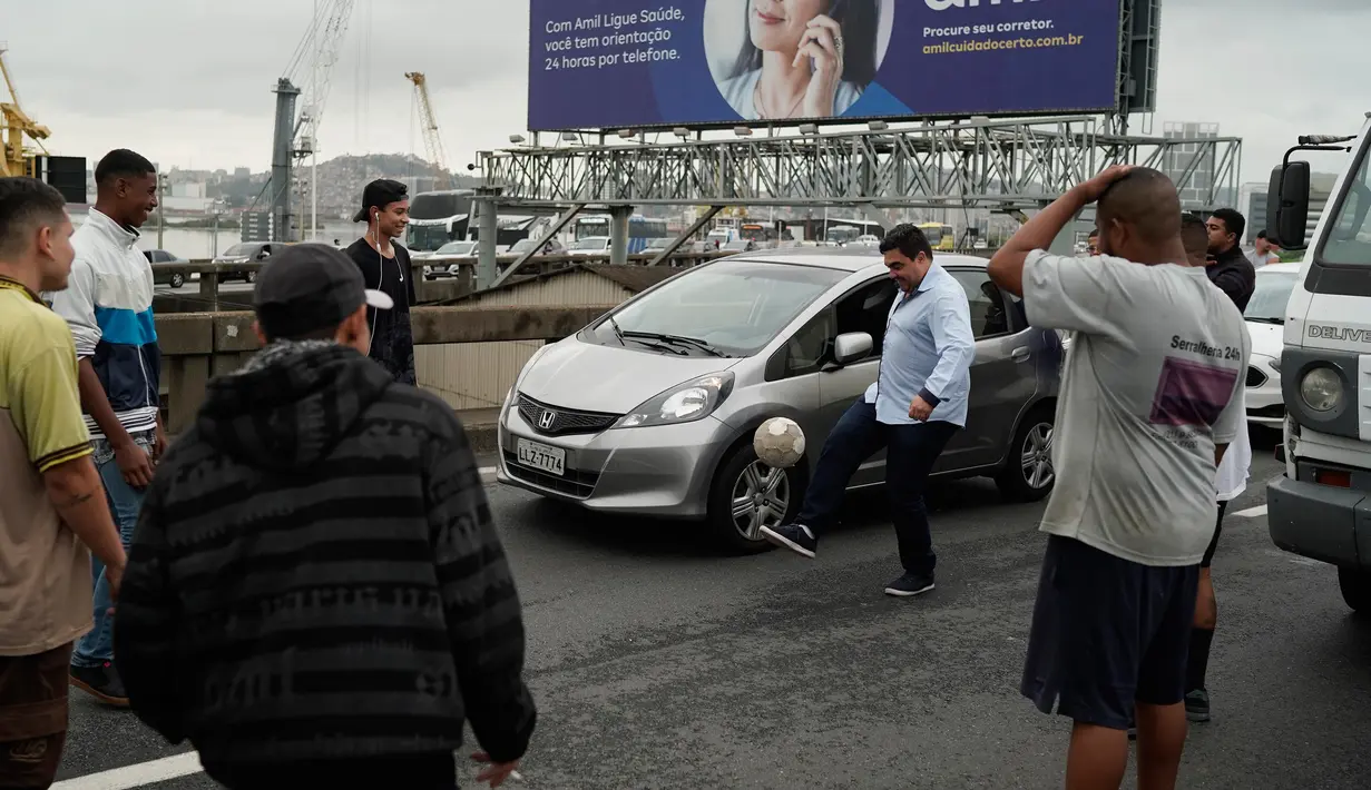 Sejumlah orang bermain bola saat lalu lintas terhenti akibat penyanderaan sebuah bus oleh seorang pria bersenjata di jembatan yang menghubungkan Kota Niteroi dengan Rio de Janeiro, Brasil, Selasa (20/8/2019). Belum diketahui motif dari penyanderaan tersebut. (AP Photo/Leo Correa)