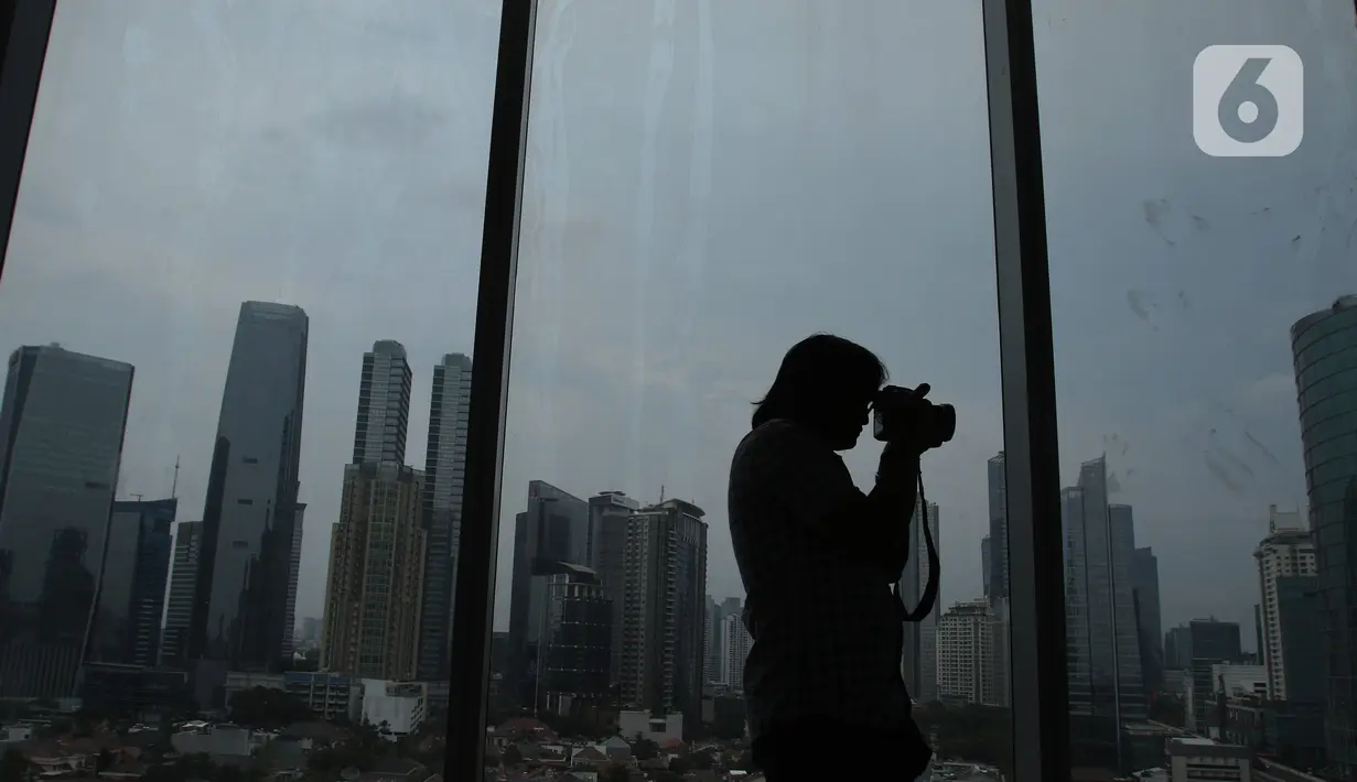 Seorang pria mengambil gambar suasana gedung bertingkat di kawsan Jakarta, Kamis (26/12/2019). Pemerintah memproyeksi pertumbuhan ekonomi tahun depan di kisaran 5,2%, berada di bawah target APBN 2020 sebesar 5,3%.  (Liputan6.com/Angga Yuniar)