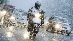 Pengendara motor melintasi hujan salju di Munich, Jerman selatan, (18/4). Hujan salju yang melanda kawasan ini tidak menyurutkan warga untuk tetap beraktivitas. (AFP PHOTO / dpa / Tobias Hase / Jerman OUT)