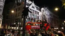 Seorang pria memanjat tiang lampu saat penggemar merayakan di atas bus di pusat kota London setelah Inggris memenangkan semifinal Euro 2020 antara Inggris dan Denmark yang dimainkan di Stadion Wembley (8/7/2021). Inggris di laga final berhadapan dengan Italia. (AP Photo/Thanassis Stavrakis)