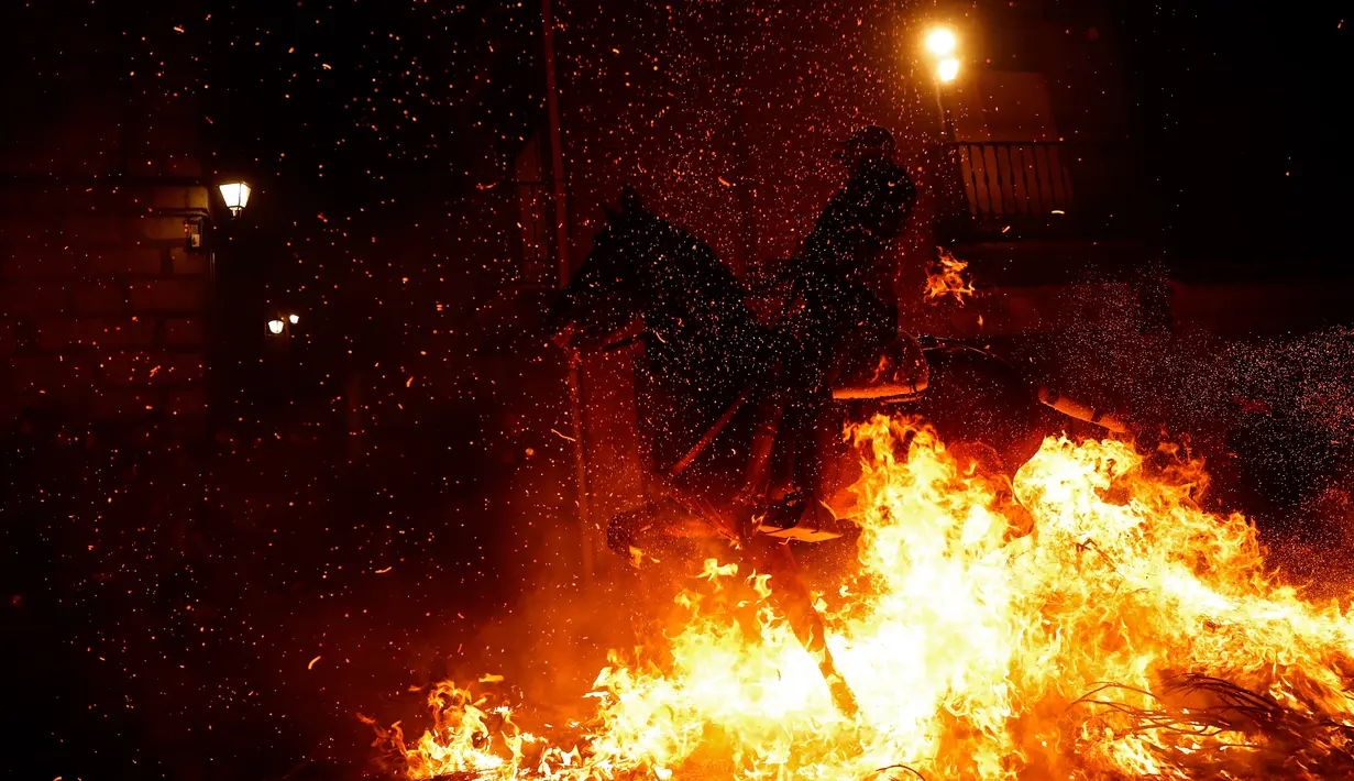 Seorang pria menunggangi kuda melewati api unggun saat festival Luminarias di San Bartolome de Pinares, Spanyol, Jumat (16/1/2020). Tradisi yang sudah berlangsung lebih dari 500 tahun ini bertujuan untuk menyucikan binatang yang identik dengan Santo Antonius. (AP Photo/Manu Fernandez)