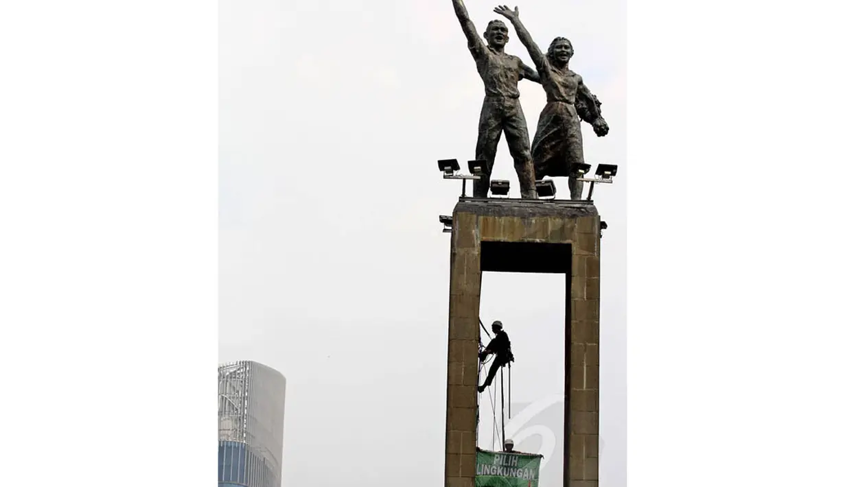 Seorang aktivis Greenpeace memanjat Tugu Selamat Datang untuk memasang spanduk bertuliskan "Pilih Presiden untuk Lingkungan" di Bundaran HI, Jakarta, Minggu (11/5/14). (Liputan6.com/Faizal Fanani)