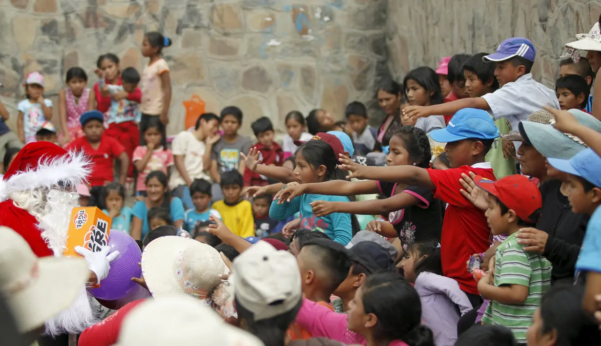 Seorang petugas polisi berpakaian seperti Santa Claus memberikan hadiah kepada anak-anak selama perayaan Natal di Huaycan, Lima, Peru (15/12/2015). (REUTERS/Janine Costa)