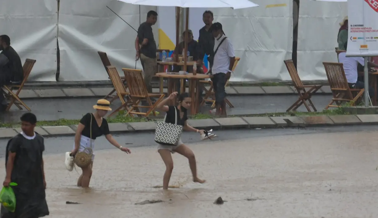 Penonton melintasi area banjir saat hujan lebat yang menyebabkan penundaan Race 1 World Superbike (WSBK) di Pertamina Mandalika International Street Circuit, Lombok Tengah, Nusa Tenggara Barat, Sabtu (20/11/2021). Hujan deras memaksa Race 1 WSBK Mandalika ditunda pada 21 November. (BAY ISMOYO/AFP)