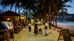 Karyawan restoran mengundang orang yang lewat saat para turis memanfaatkan program "Kotak Pasir Phuket" untuk pengunjung yang divaksinasi penuh terhadap virus corona Covid-19 di pulau Phuket Thailand (25/10/2021). (AFP/Mladen Antonov)