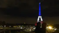  Sepasang kekasih berdiri dengan latar belakang Menara Eiffel yang dihiasi lampu berwarna bendera Prancis merah, putih dan biru, untuk menghormati para korban serangan teror di Paris pada 13 November 2015 lalu, Senin (16/11). (AFP PHOTO/LUDOVIC MARIN)