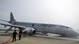 Petugas pemadam kebakaran menyemprotkan air ke pesawat Myanmar National Airline (MNA) yang mendarat tanpa roda depan di Bandara Internasional Mandalay, Myanmar, Minggu 12 Mei 2019. Kejadian ini tidak menyebabkan 82 penumpang serta tujuh kru terluka. (Aung Thura via AP)