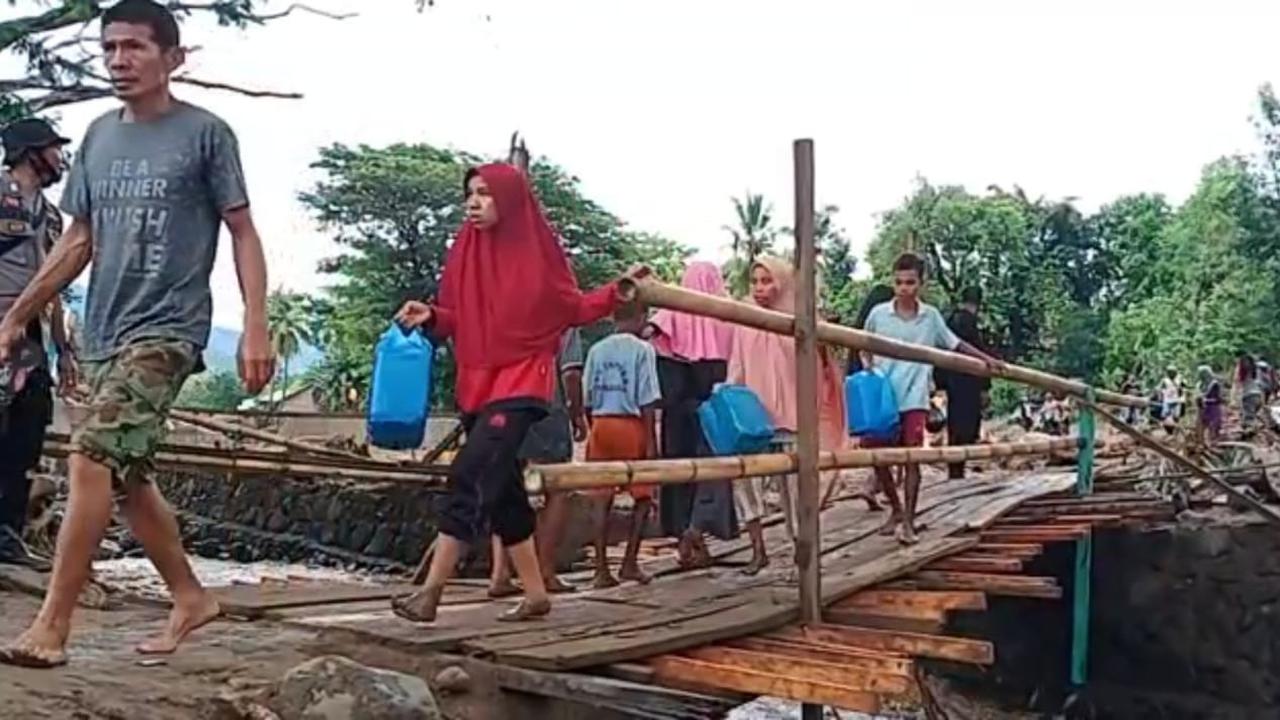 Warga Desa Waiburak, melintasi jembatan darurat yang dibangun TNI/Polri pasca banjir bandang untuk membelih minyak tana di Kelurahan Waiwerang. (Liputan6.com/Dionisius Wilibardus)