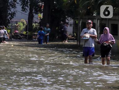 Warga melintasi genangan air yang merendam jalan di kawasan Kampung Makasar, Jakarta Timur, Senin (7/7/2025). (Liputan6.com/Herman Zakharia)