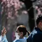 Pengunjung mengenakan masker wajah di tengah kekhawatiran akan penyebaran Virus Corona COVID-19 di hadapan pohon ceri di Taman Ueno Tokyo Jepang pada 12 Maret 2020. (Philip FONG / AFP)