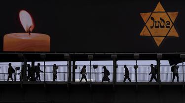 Orang-orang berjalan melewati jembatan yang diterangi dengan papan reklame bergambar Bintang Daud kuning bertuliskan "Jude", Yahudi dalam bahasa Jerman, menyerupai yang dikenakan oleh orang-orang Yahudi di Nazi Jerman saat Hari Peringatan Holocaust tahunan di Ramat Gan, Israel, 28 April 2022. Israel memperingati Hari Peringatan Holocaust tahunan bagi enam juta orang Yahudi yang menjadi korban genosida Nazi selama Perang Dunia II. (AP Photo/Oded Balilty)