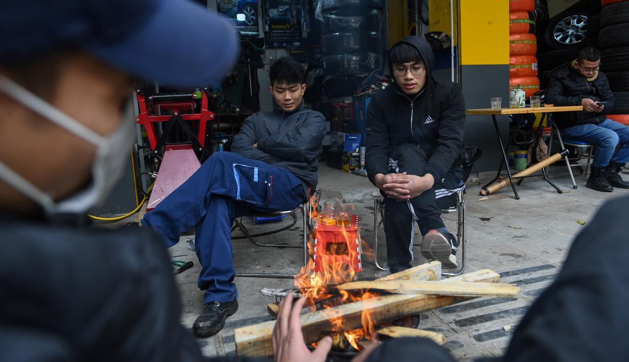 Orang-orang menghangatkan diri dengan kayu bakar pada hari yang dingin di luar toko ban di Hanoi, Jumat (8/1/2021). Vietnam tahun ini diperkirakan mengalami musim dingin yang lebih dingin dari biasanya ketika suhu permukaan laut Samudra Pasifik turun, membentuk fenomena La Nina. (Nhac NGUYEN/AFP)
