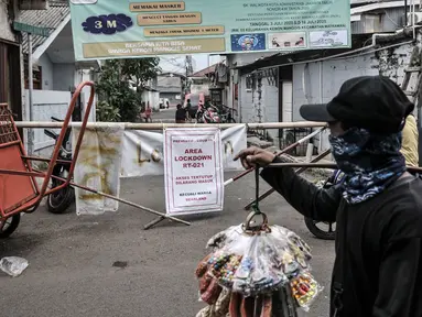 Pedagang melintas di depan jalan permukiman yang ditutup usai ditetapkan sebagai Zona Merah Covid-19 di RW 03 Kelurahan Kebon Manggis, Jakarta, Selasa (14/7/2020). Jumlah RW yang masuk dalam zona merah Covid-19 di DKI Jakarta kembali bertambah menjadi 30 RW. (Mmerdeka.com/Iqbal Nugroho)