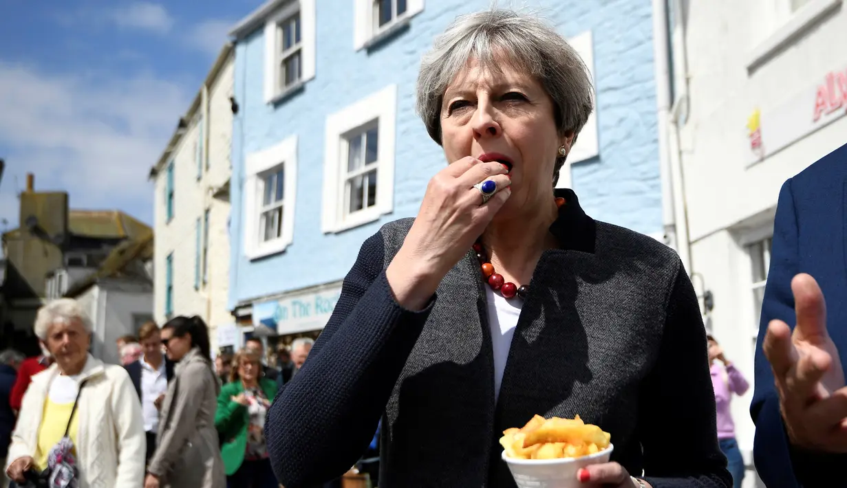 Perdana Menteri (PM) Inggris, Theresa May mencicipi beberapa keripik saat berhenti untuk kampanye di Mevagissey, Cornwall, Selasa (2/5). Theresa May melakukan kampanye dengan berkeliling jalanan di Cornwall. (Dylan Martinez/PA via AP)