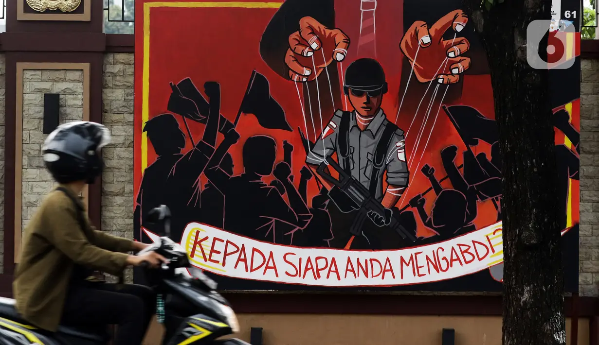 Pengendara melintas di depan mural berisi kritik terhadap kinerja polisi di Lapangan Bhayangkara Mabes Polri, Jakarta, Minggu (31/10/2021). Lomba mural 2021 Piala Kapolri menampilkan sejumlah karya berisi kritik terhadap polisi yang dituangkan pada media triplek. (Liputan6.com/Helmi Fithriansyah)