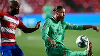 Bek Real Madrid, Sergio Ramos menendang bola dari kawalan pemain Granada, Dimitri Foulquier pada pertandingan lanjutan La Liga Spanyol  di stadion Nuevo Los Carmenes di Granada (13/7/2020). Madrid menang tipis 2-1 atas Granada. (AP Photo/Jose Breton)