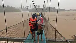 Tim penyelamat membantu warga menyeberangi jembatan saat dievakuasi di kota Tubay, Agusan del Norte, Filipina selatan, Kamis (16/12/2021). Puluhan ribu orang sedang dievakuasi ke tempat yang aman ketika Topan Rai mendekati pada Kamis (16/12). (Philippine Coast Guard via AP)