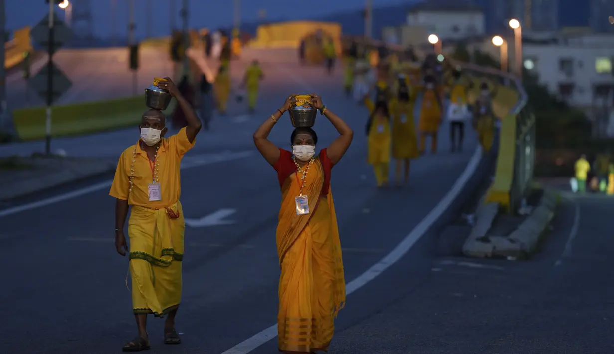 Umat Hindu mengenakan masker membawa teko susu dalam prosesi selama festival Thaipusam sebagai umat mematuhi prosedur operasi standar yang ketat karena pandemi COVID-19 di Gua Batu di pinggiran Kuala Lumpur, Malaysia, Selasa (18/1/2022). (AP Photo/ Vincent Thian)