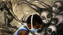 Seorang anak yang mengenakan masker lewat di depan mural berjudul ‘Marcha Hacia la Oscuridad’ atau ‘Move Toward Darkness’ karya seniman Yulier P. di Havana, Kuba, Jumat (10/4/2020). Yulier P. mengatakan muralnya menunjukkan ketidakberdayaan manusia menghadapi COVID-19. (AP Photo/Ramon Espinosa)