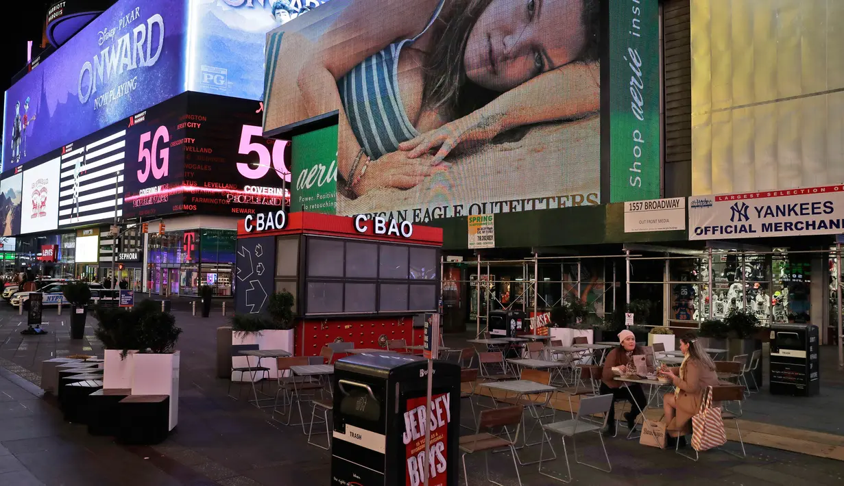 Dua wanita duduk di Times Square di New York, Senin, (16/3/2020). Tiga wilayah juga akan membatasi kapasitas kerumunan untuk pertemuan sosial dan rekreasi hingga 50 orang. (AP Photo/Seth Wenig)