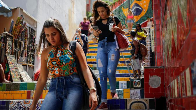 Pejalan kaki melintasi anak tangga yang terkenal dengan nama Selaron Steps atau Escadaria Selarón di Rio de Janeiro, Brasil pada 9 Desember 2019. Sang seniman pembuat yang bernama Jorge Selaron mempersembahkan karya seninya untuk rakyat Brasil. (Photo by David GANNON / AFP)