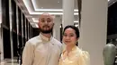 Rachel Amanda tampil anggun kenakan dress warna kuning dengan sentuhan vintage yang terlihat pada detail puff di lengan. Ia hadir bersama suaminya yang mengenakan top bersiluet surjan warna putih. [@auroraamanda95].