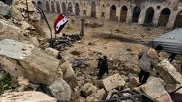 Anggota pasukan Presiden Suriah Bashar al-Assad, mengibarkan bendera Suriah di antara puing bangunan yang hancur karena gempuran senjata selama perang saudara berlangsung, di kompleks Masjid Umayyad, Aleppo, 13 Desember 2016. (REUTERS/Omar Sanadiki)