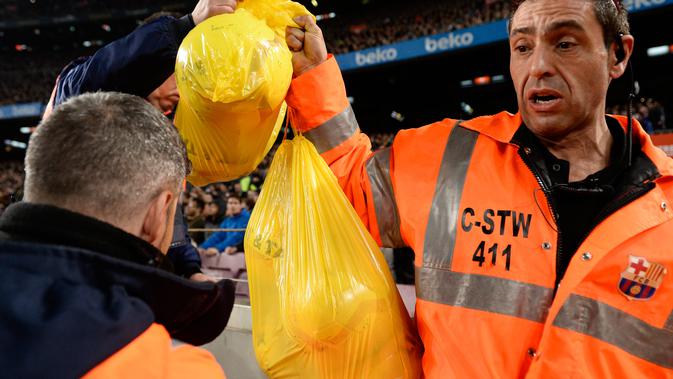 Petugas memungut bola yang dilemparkan simpatisan Tsunami Democratic ke lapangan saat Barcelona bertemu Real Madrid di Camp Nou, Rabu (18/12/2019) (Josep Lago / AFP)