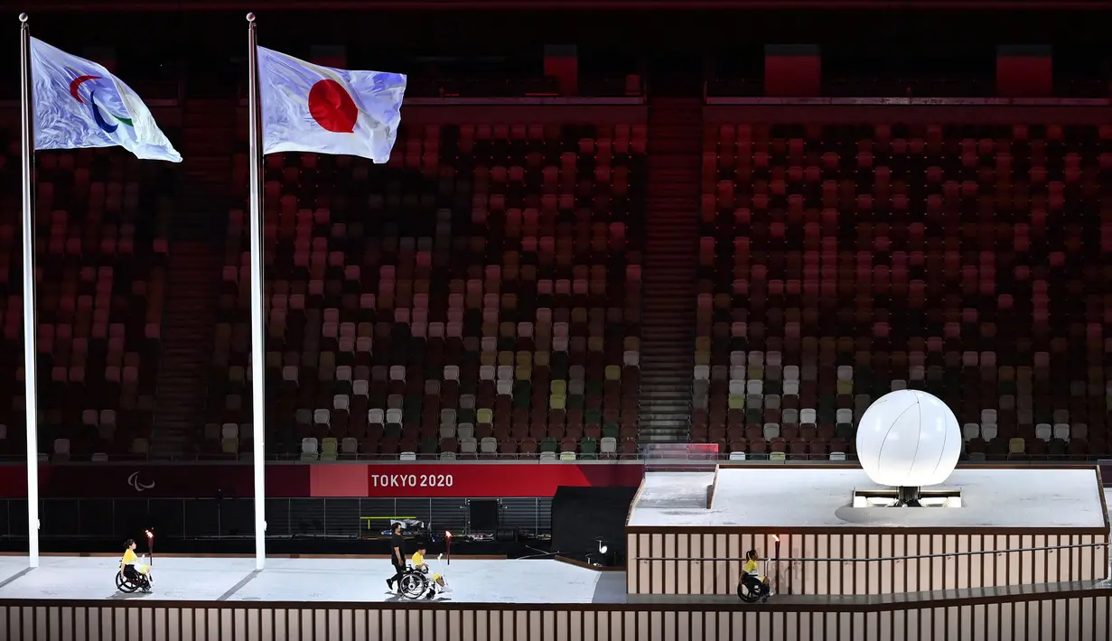 Tiga pembawa obor mengangkut api Paralimpiade sebelum menyalakan kuali (kanan) selama upacara pembukaan Paralimpiade Tokyo 2020 di Stadion Olimpiade di Tokyo pada 24 Agustus 2021. (AFP/Charly Triballeau)