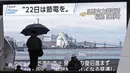 Orang-orang berjalan di depan monitor besar program berita yang menyerukan penghematan listrik di Tokyo, Selasa (22/3/2022). Pemerintah Jepang memperingatkan potensi pemadaman karena kekurangan pasokan listrik akibat tutupnya beberapa pembangkit setelah gempa bumi pekan lalu. (Kyodo News via AP)