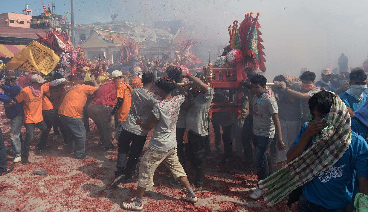 Warga keturunan Thailand-China mengarak kereta kayu yang membawa patung Dewi serta menyalakan petasan saat merayakan festival keagamaan tahunan di distrik Sungai Kolok, Thailand (8/5). (AFP/Madaree Tohlala)