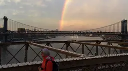 Warga beraktivitas saat pelangi terlihat dari Jembatan Brooklyn di New York City, AS (15/5). Jembatan ini adalah jembatan suspensi terpanjang di dunia sejak pembukaannya hingga 1903, serta jembatan suspensi kabel baja pertama. (AFP Photo/Hector Retamal)