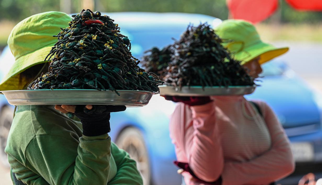 Pedagang Kamboja membawa tarantula goreng dan jangkrik di kota Skun di provinsi Kampong Cham pada 15 Januari 2023. Tarantula merupakan salah satu makanan favorit nan lezat di Kamboja, tepatnya di wilayah Skun. (Photo by TANG CHHIN SOTHY / AFP)