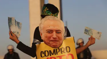 Seorang wanita memegang uang palsu dan poster bergambar Presiden Brasil Michel Temer pada unjuk rasa di depan Kongres Nasional, Brasilia, Rabu (2/8). Para demonstran membanjiri jalanan kota sejak Rabu waktu setempat. (AP/Eraldo Peres)