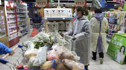 Seorang wanita mengenakan jas hujan dan masker membeli makanan di sebuah supermarket di Wuhan di provinsi Hubei, China tengah, Senin, (10/2/2020). China melaporkan kenaikan angka kematian akibat wabah virus corona. (Chinatopix via AP)