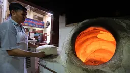 Tukang roti bersiap memasukkan adonan roti Iran atau taftoon ke dalam oven tradisional di sebuah toko di Kuwait City, Kuwait, 27 Juni 2019. Pembuat roti menaruh adonan di atas bantal untuk kemudian ditempelkannya ke dinding oven tradisional yang terbuat dari tanah liat. (YASSER AL-ZAYYAT/AFP)