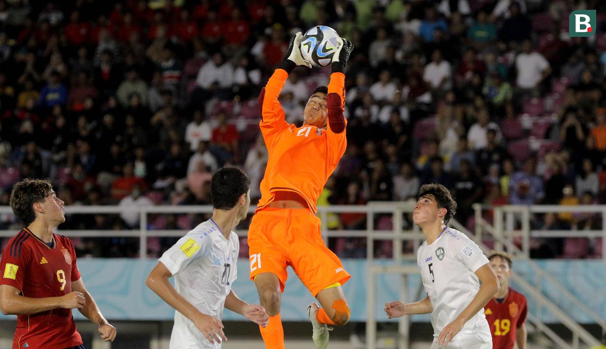 Kiper Timnas Uzbekistan U-17, Muhammadyusuf Sobirov, mengamankan bola tendangan pemain Spanyol U-17 dalam pertandingan babak penyisihan Grup B Piala Dunia U-17 di Stadion Manahan, Solo. Kamis (16/11/2023). (Bola.com/Arief Bagus)