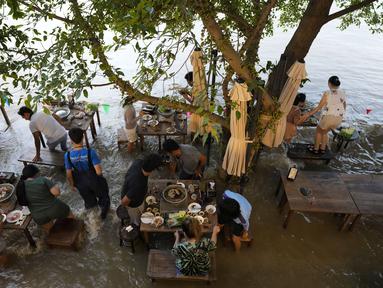 Pelanggan Chaopraya Antique Café di tepi sungai menikmati ketinggian air di Sungai Chao Phraya dekat Bangkok, Thailand, Kamis (7/10/2021). Restoran yang dilanda banjir ini menjadi tempat makan tidak biasa di mana pengunjung menikmati santapan makanan dengan kaki terendam. (AP Photo/Sakchai Lalit)
