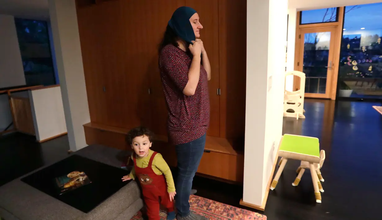 Nadia Chaouch mengenakan jilbab dalam persiapan untuk salat ketika putranya Yusuf Kamel berjalan melewati setelah keluarga berbuka puasa pada bulan sucir Ramadan di rumah mereka selama wabah coronavirus di Seattle (28/4/2020). (AP/Elaine Thompson)