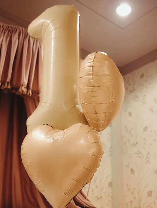 Balon angka satu berukuran besar dipadukan dengan balon hati menjadi focal point, sementara boneka kelinci, buket bunga peony berwarna pink, serta kain rajut pastel membuat suasana terasa hangat dan dreamy. [@alyssadaguise].