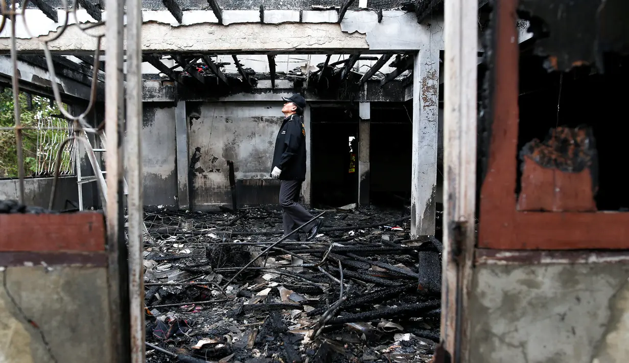 Seorang polisi memeriksa bangunan asrama sekolah yang hangus terbakar di Thailand utara, Senin (23/5). 17 siswi tewas setelah kebakaran menghanguskan asrama sekolah untuk anak-anak suku pedalaman miskin itu. (REUTERS/Athit Perawongmetha)