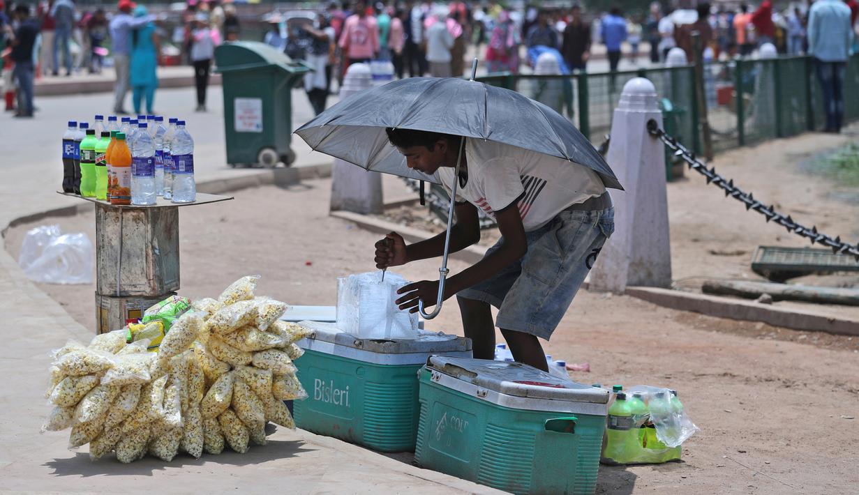 Seorang penjual makanan menggunakan payung selama musim panas di New Delhi, India (10/6/2019). Kondisi gelombang panas yang parah menyapu bagian utara dan barat India dengan suhu maksimum melonjak hingga 48 derajat Celcius ( 118 F) di beberapa bagian Rajasthan. (AP Photo/Manish Swarup)
