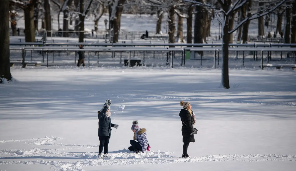 Sebuah keluarga berdiri di lapangan tertutup salju di Central Park setelah badai salju pertama musim dingin 2022 di New York City, Jumat (7/1/2022). Badai musim dingin membawa lebih dari 15 cm salju di bagian timur Amerika Serikat (AS), menutup sekolah, kantor dan jalan-jalan. (Ed JONES / AFP)
