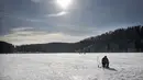 Seorang pria memancing melalui lubang es di danau beku yang tertutup salju dekat Vilnius, Lithuania, Minggu (13/2/2022). Suhu udara 0 derajat Celcius (32 derajat Fahrenheit). (AP Photo/Mindaugas Kulbis)