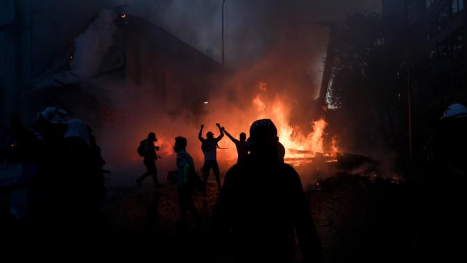 Para pengunjuk rasa berdiri di luar puing-puing gereja Parroquia La Asuncion yang dibakar sekelompok orang di Kota Santiago, Chile, Minggu (18/10/2020). Demonstrasi itu digelar untuk memperingati satu tahun protes besar menuntut kesetaraan di Chile. (AP Photo/Esteban Felix)