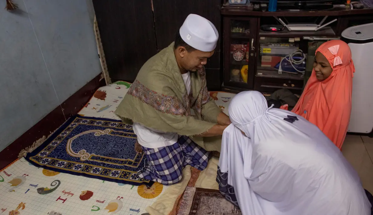 Seorang perempuan Thailand mencium tangan suaminya setelah salat di ruang tamu rumah mereka di Bangkok, 28 April 2020. Banyak tempat ibadah ditutup guna membendung penyebaran Virus Corona COVID-19 ketika Umat Muslim di seluruh dunia menyambut bulan suci Ramadan. (AP Photo/Gemunu Amarasinghe)