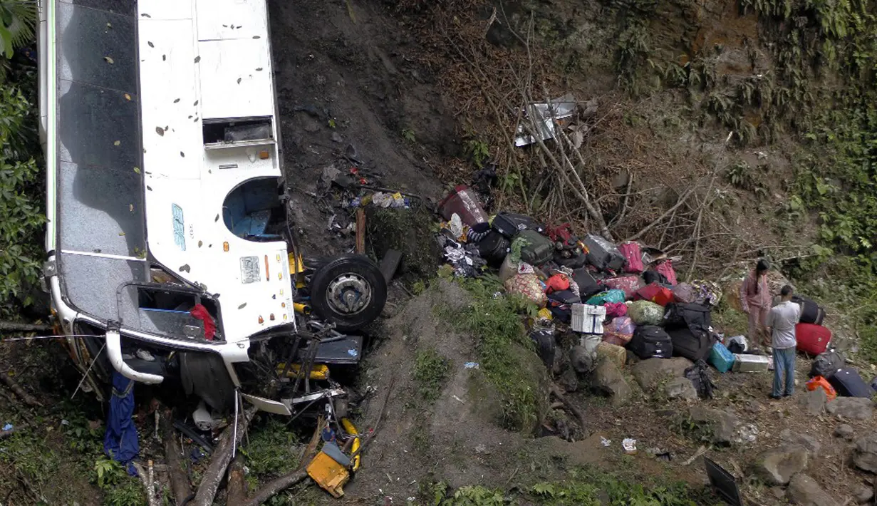 Warga berusaha mengambil barang-barang mereka dekat bus yang jatuh di jalan penghubung Medellin dan Bogota dekat San Luis, Provinsi Antiokia, Kolombia, 27 Desember 2021. Tujuh orang, termasuk seorang wanita hamil, tewas dan 20 lainnya luka-luka ketika sebuah bus terjun ke jurang. (Fredy BUILES/AFP)